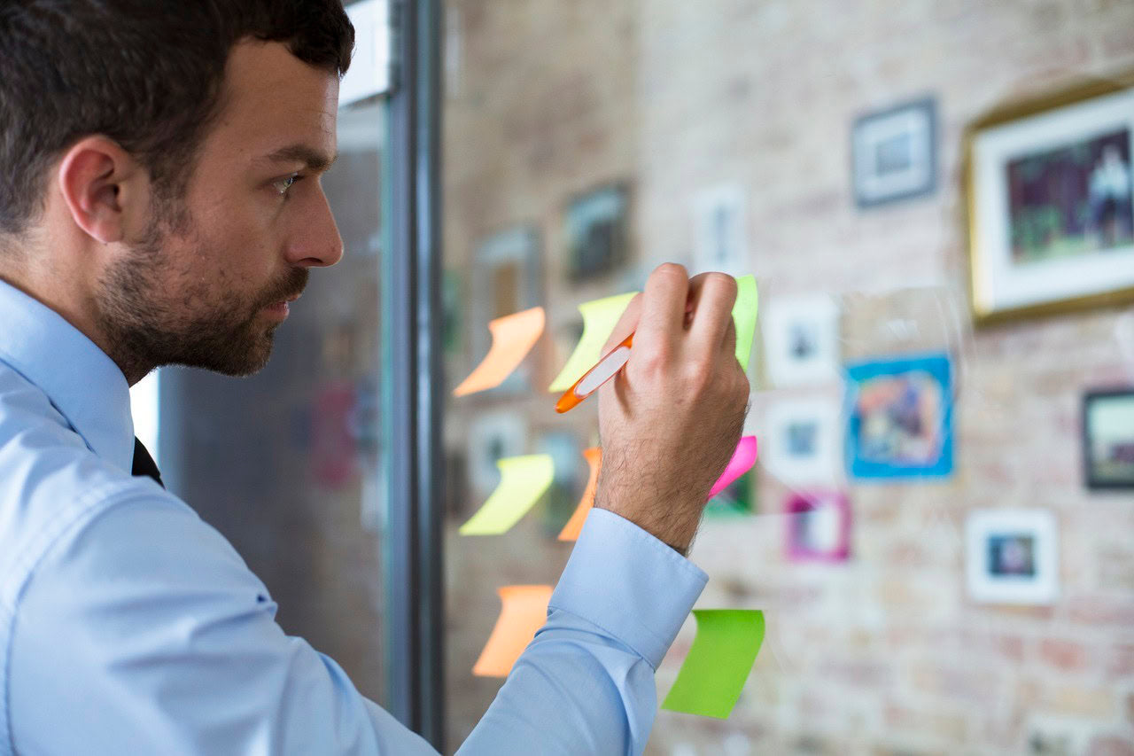 Businessman in office writing on adhesive note on glass wall