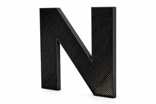 Letra corpórea impresa en 3D PLA inclinada con frontal de lineas negras y trasera blanca en fondo blanco